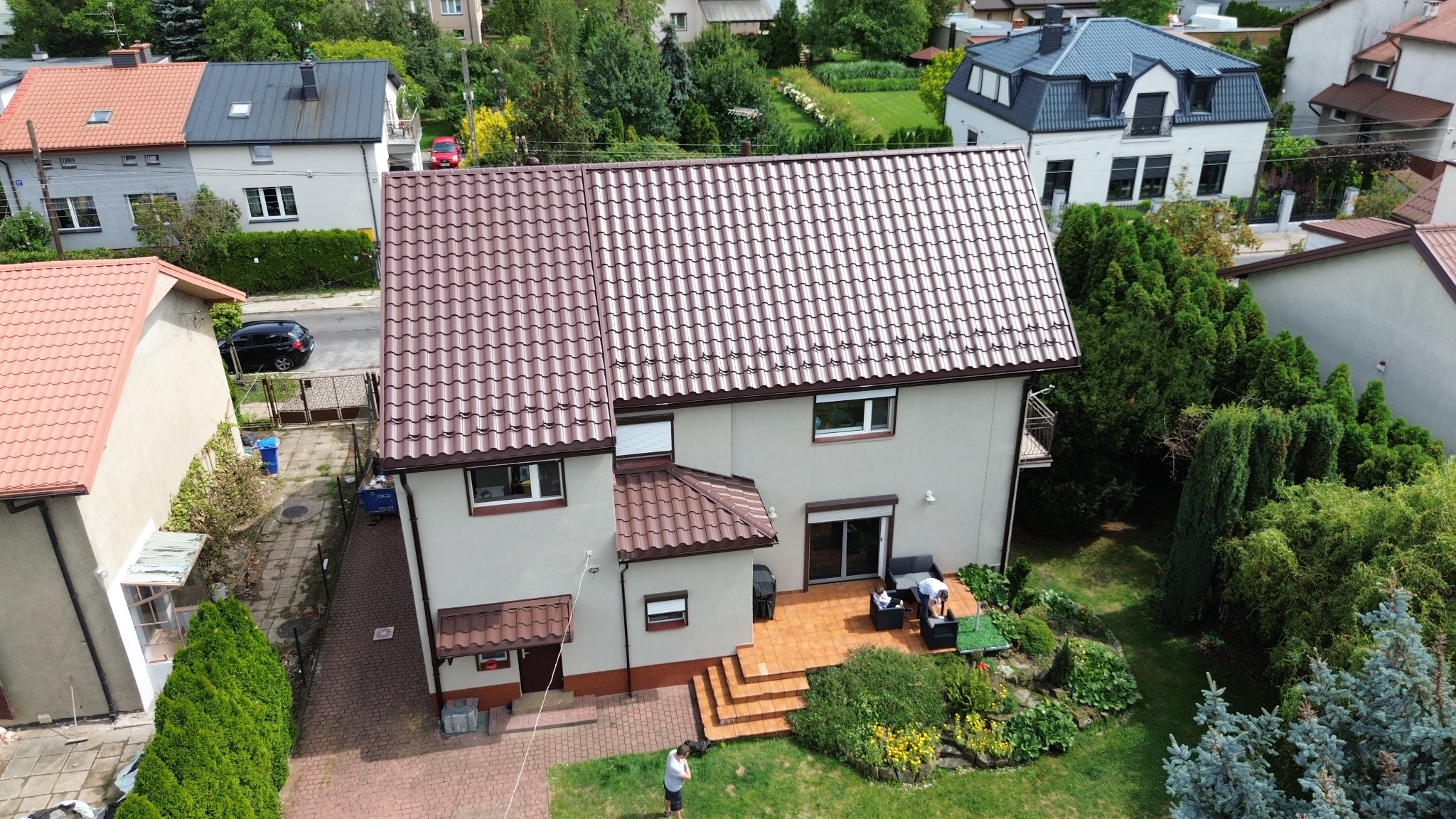 Dom jednorodzinny z nowym, brązowym dachem z blachodachówki, widok z góry na ogród i taras z meblami ogrodowymi.