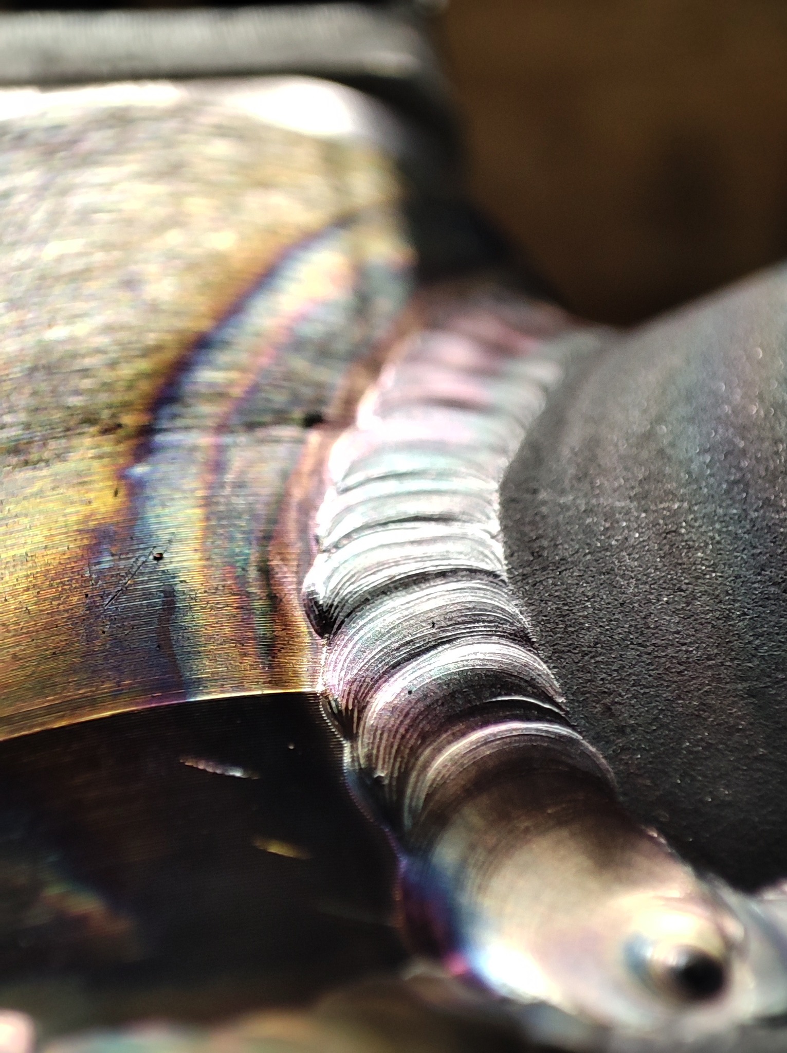 Zbliżenie spawu z widocznymi tęczowymi przebarwieniami na metalu, ukazujące precyzyjne nałożenie kolejnych warstw spoiny.