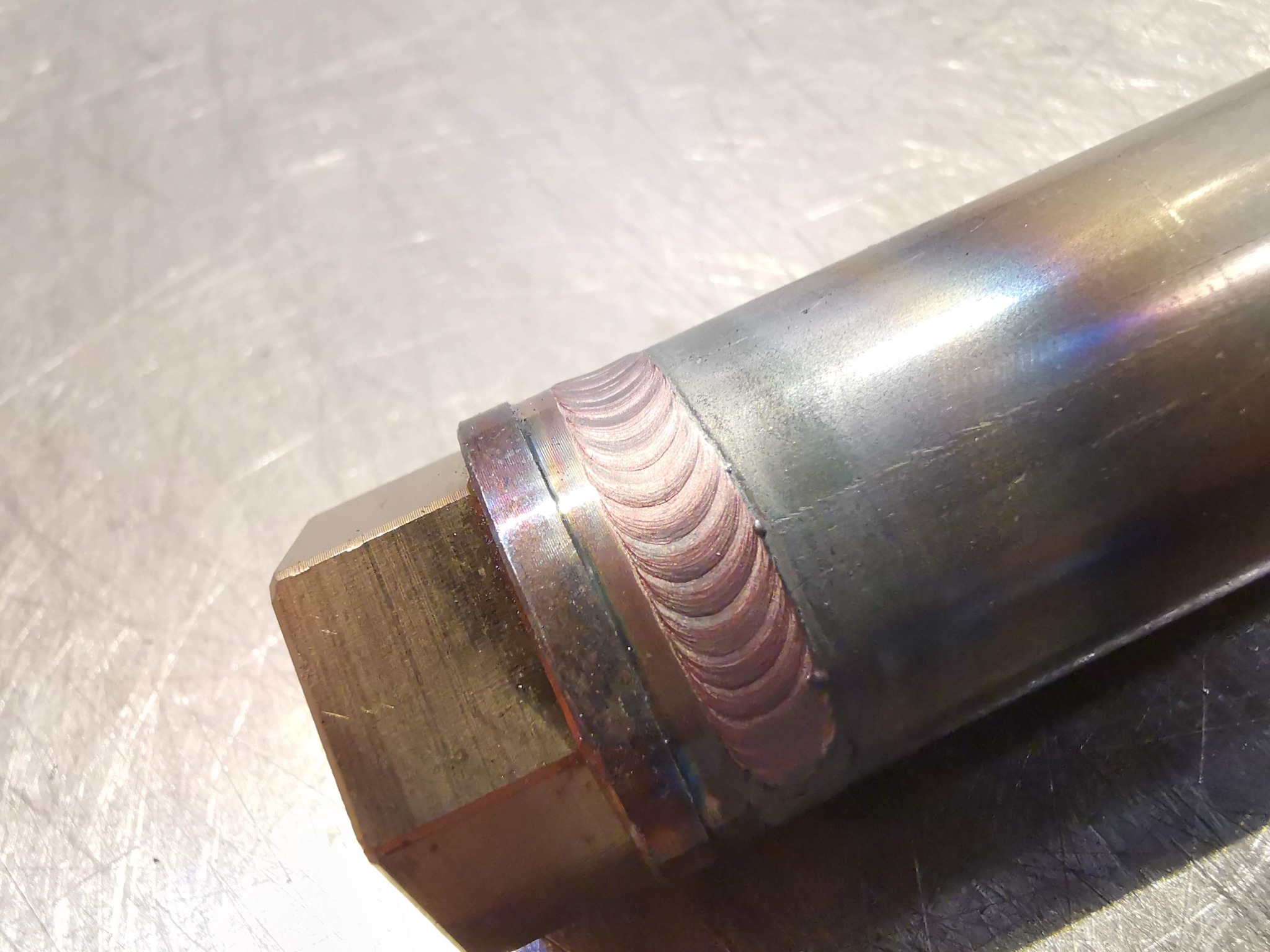 Precyzyjne spawy łączące element sześciokątny z rurą, widoczne opalizujące przebarwienia termiczne na spoinie.