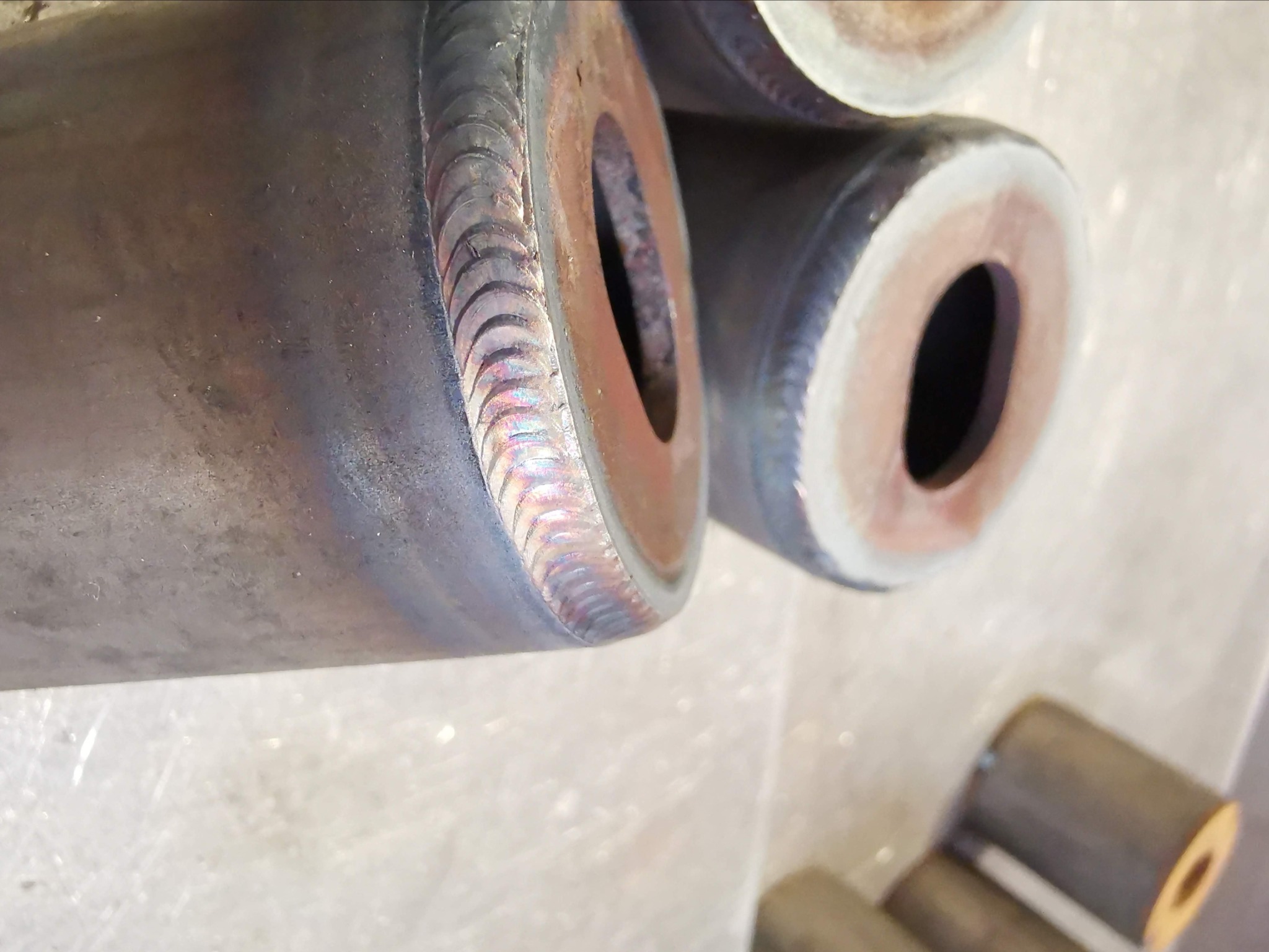 Metalowe rury z precyzyjnymi spawami, widoczne ślady obróbki termicznej i otwory, ułożone na jasnej powierzchni roboczej.