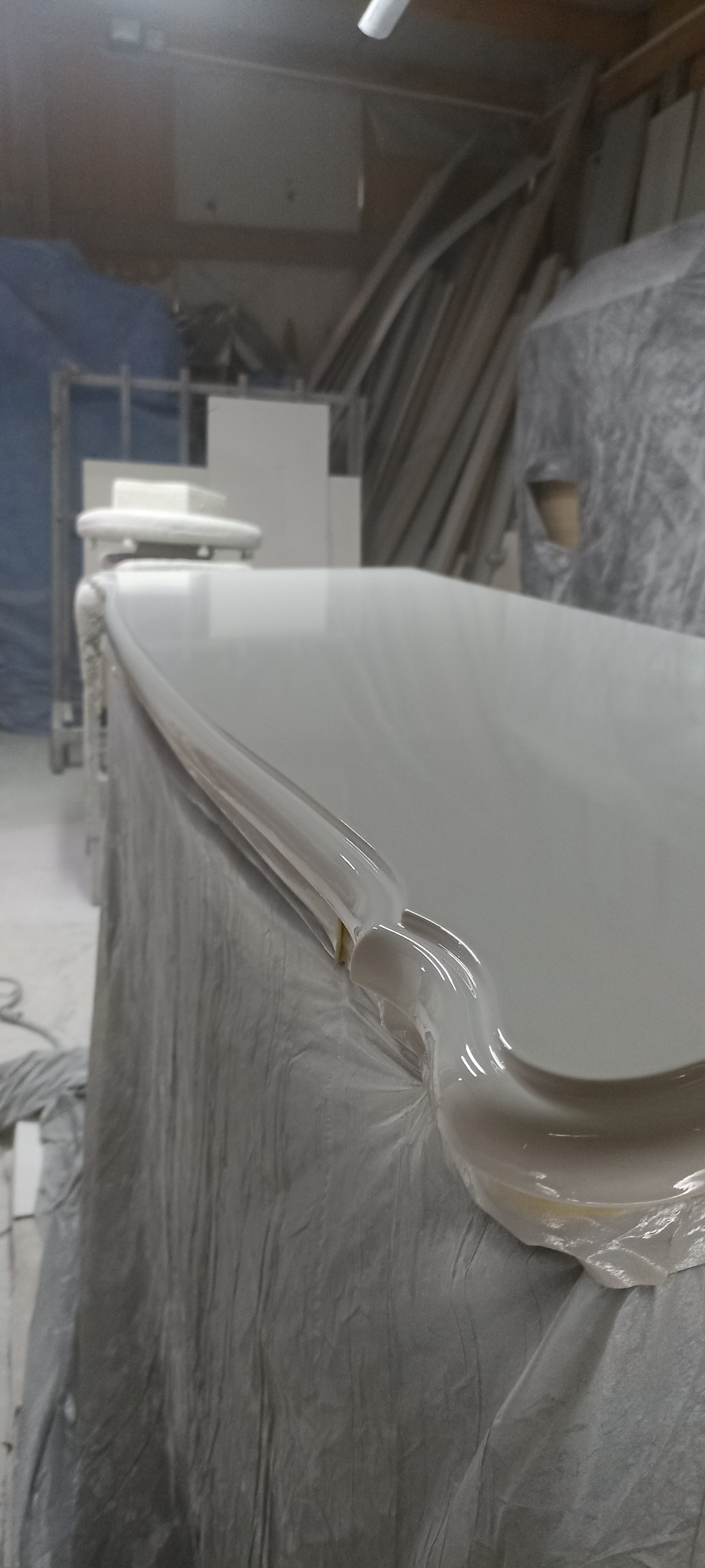 Błyszcząca, świeżo polakierowana komoda w trakcie renowacji, zabezpieczona folią ochronną w warsztacie stolarskim.