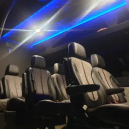 Wnętrze luksusowego busa z szarymi skórzanymi fotelami z podłokietnikami i niebieskim oświetleniem sufitowym w romby.