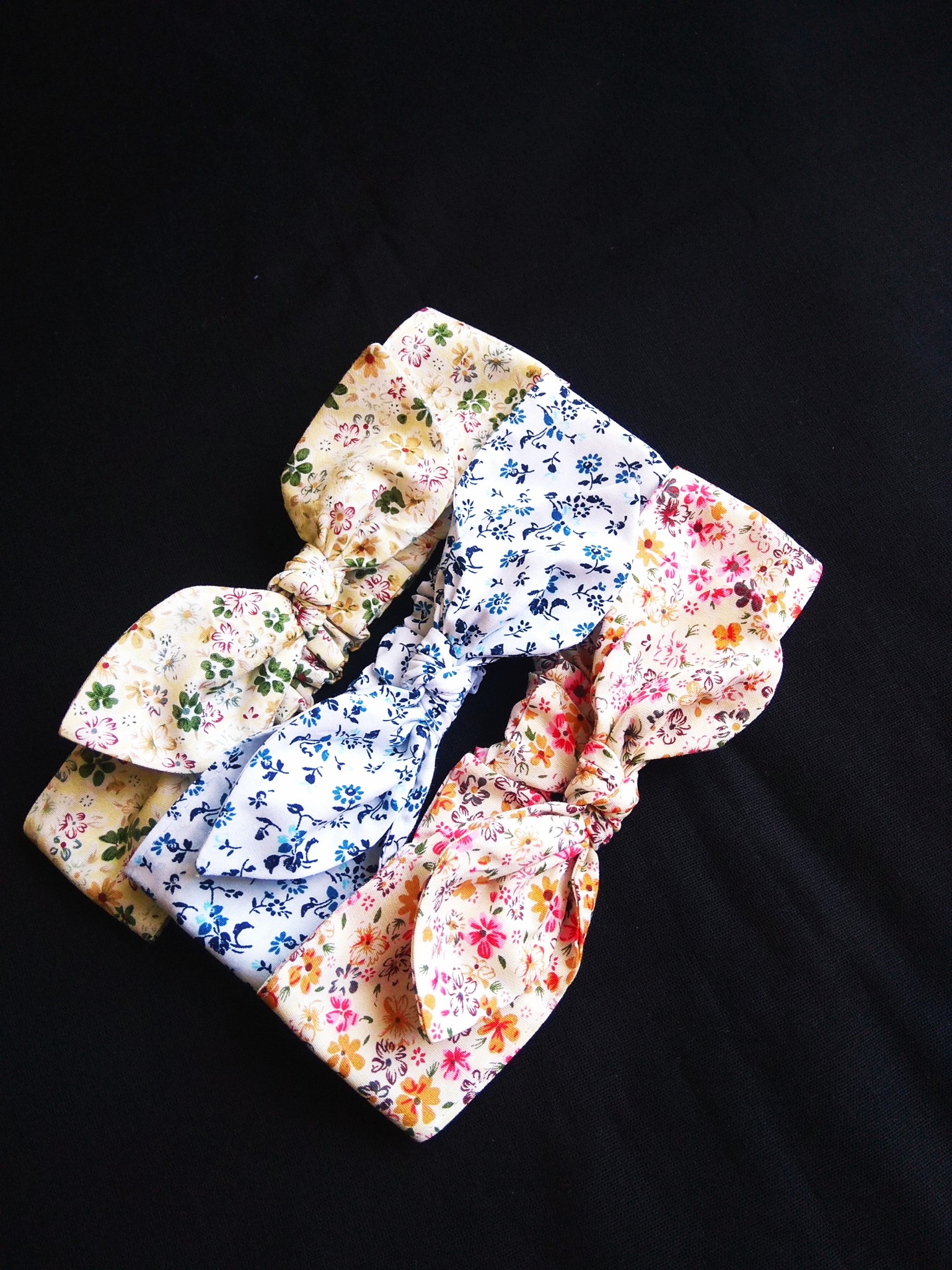 Trzy ręcznie robione opaski do włosów z motywami kwiatowymi, ułożone na czarnym tle w Malborku. Opaski mają różne wzory: kremowy z czerwonymi i zielonymi kwiatami, biały z niebieskimi kwiatami,...