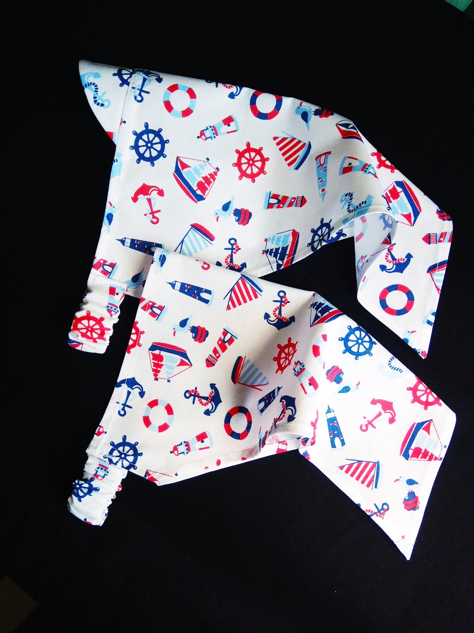 Dwie białe, bawełniane chustki dziecięce z nadrukiem w motywy marynistyczne (kotwice, koła sterowe, boje ratunkowe, latarnie morskie) na czarnym tle.
