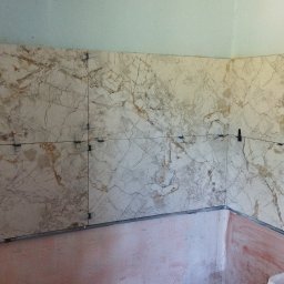 Bud - Ściana w trakcie obkładania marmurkowymi płytkami, widoczne krzyżyki dystansowe i linia pomocnicza, dolna część ściany przygotowana pod płytki.