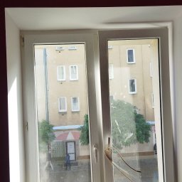 Bud - Wnętrze z widokiem na ulicę przez białe, dwuskrzydłowe okno PCV; ściana pomalowana na ciemny fiolet, widoczne ślady po naklejkach na szybie.