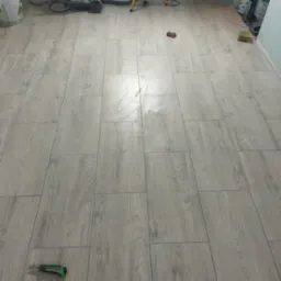 Ułożone panele podłogowe imitujące drewno, widoczny nóż do cięcia paneli, gąbka i inne narzędzia w tle.