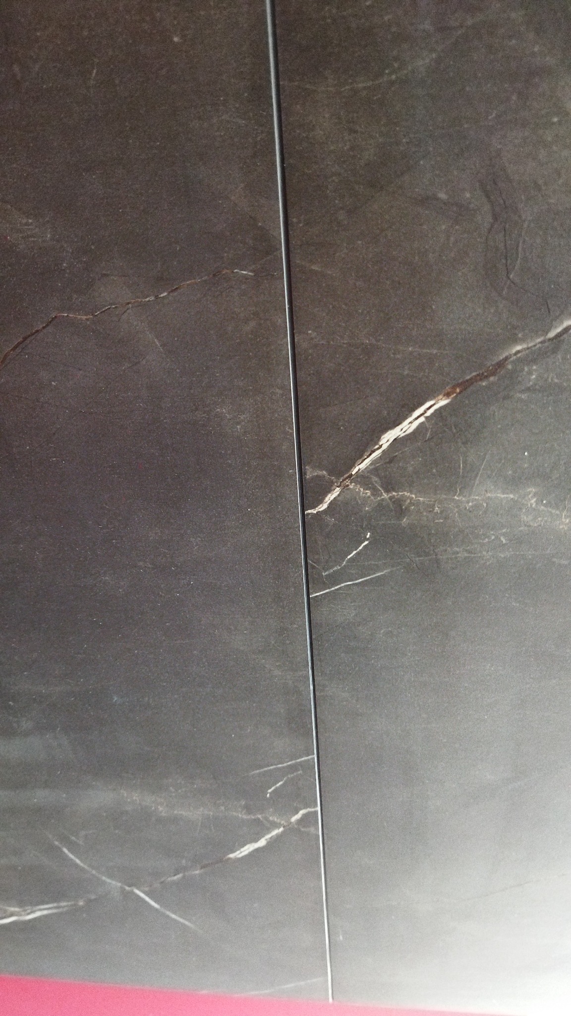 Ciemne, marmurowe płytki z wyraźnym, białym użyleniem, ułożone z wąską fugą.