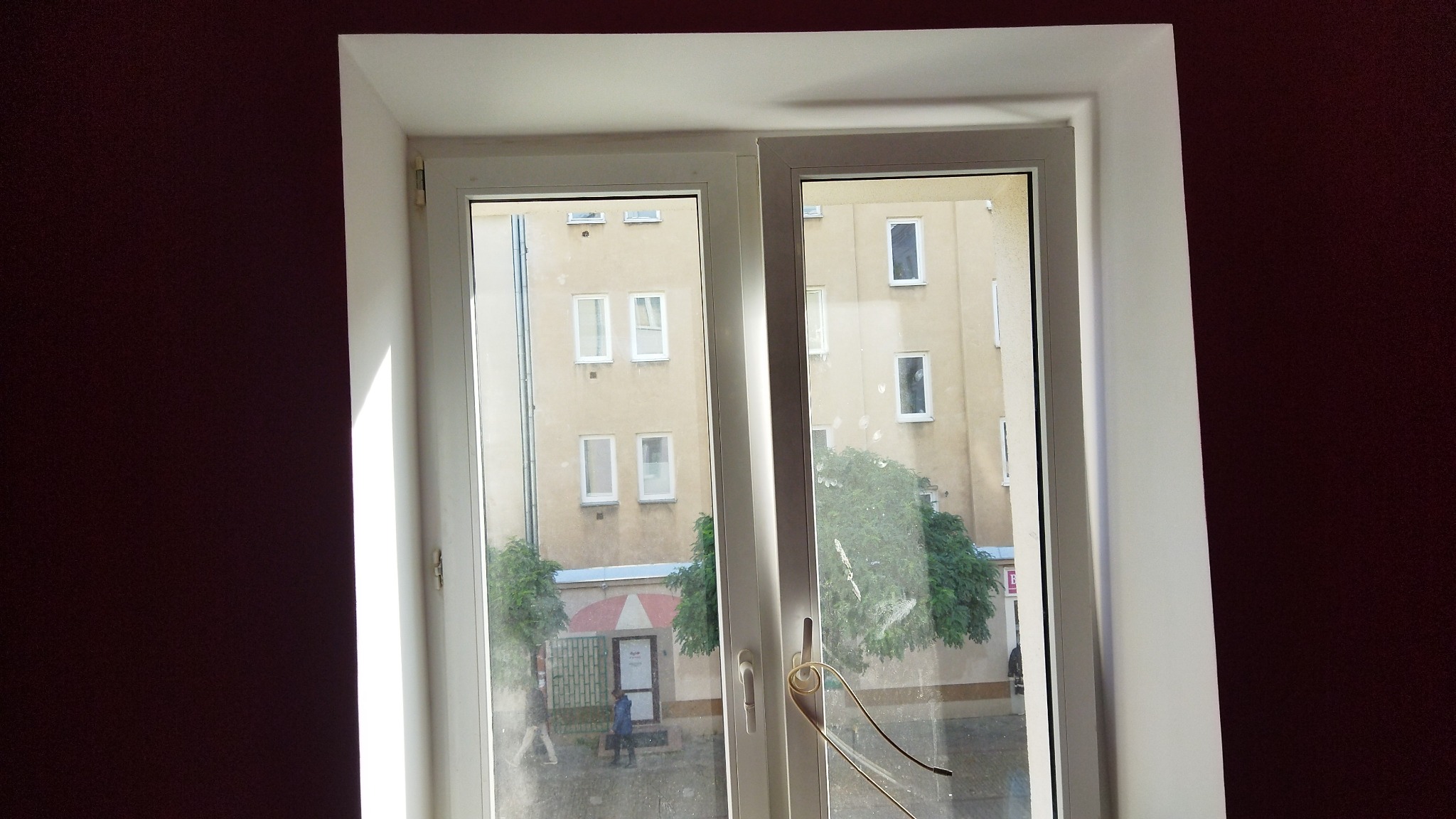 Wnętrze z widokiem na ulicę przez białe, dwuskrzydłowe okno PCV; ściana pomalowana na ciemny fiolet, widoczne ślady po naklejkach na szybie.