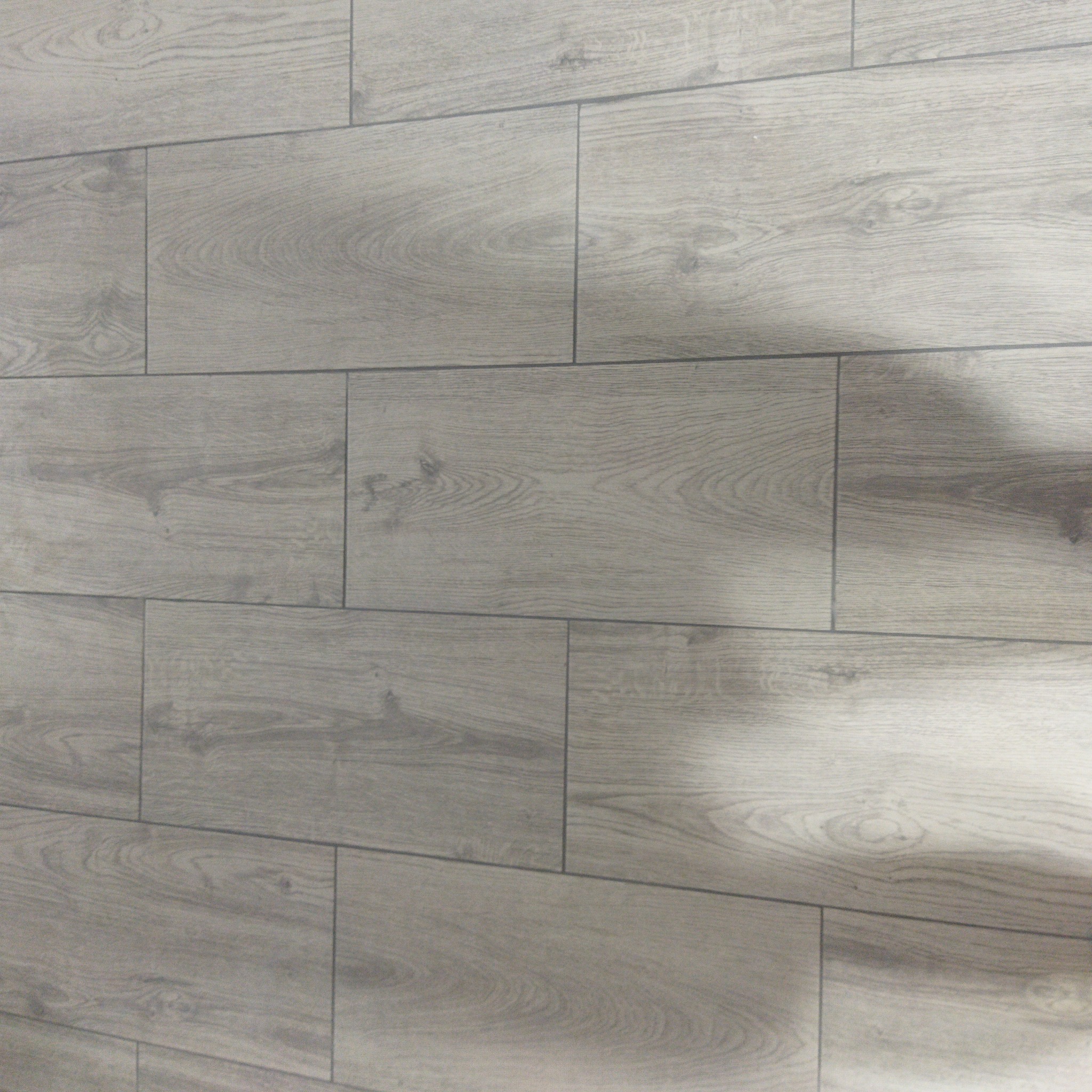 Jasnoszare panele podłogowe z wyraźnym wzorem drewna ułożone na podłodze, widoczne z boku.