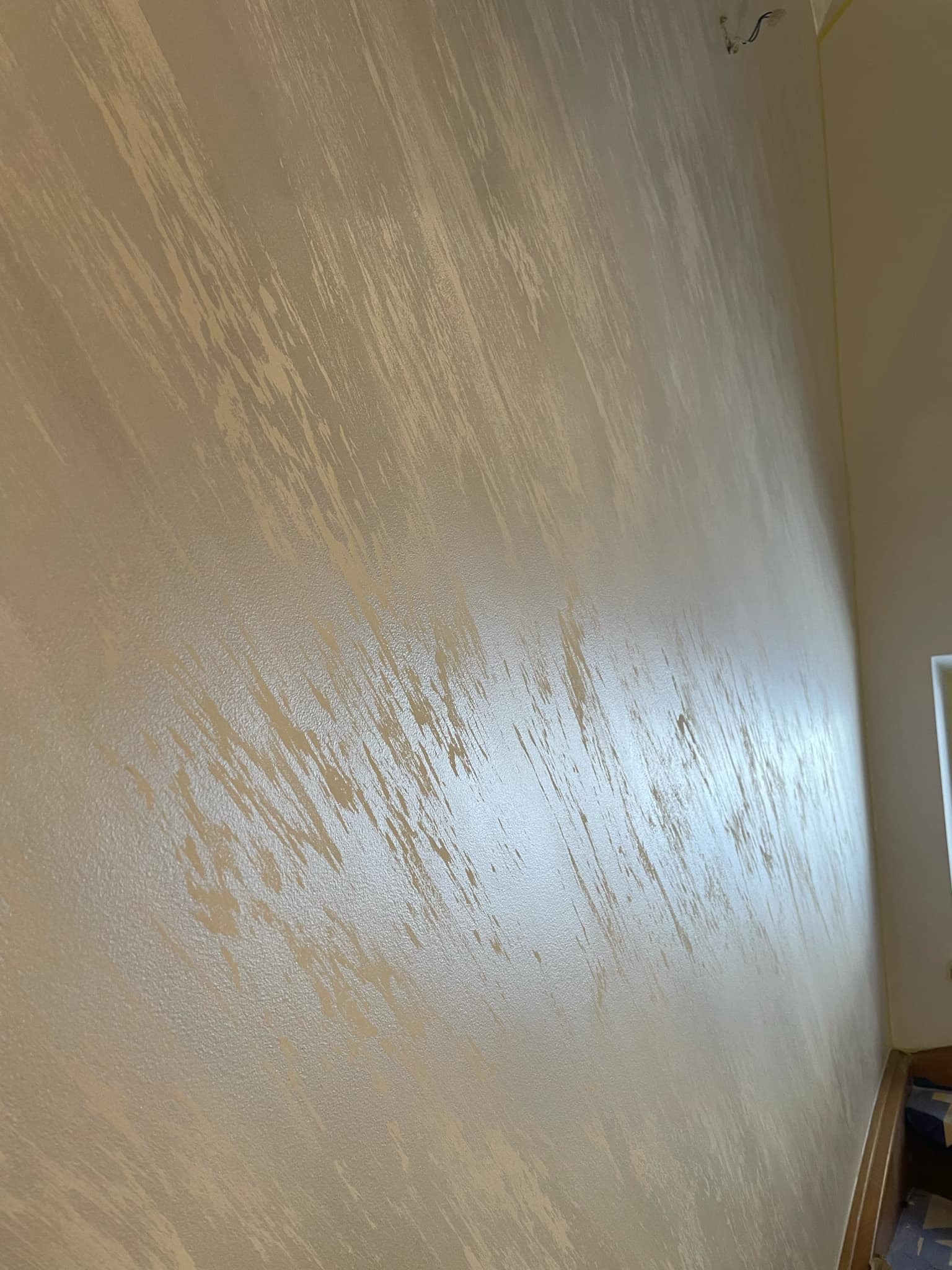 Ściana pokryta dekoracyjną, beżowo-złotą farbą o fakturze imitującej pociągnięcia pędzlem, widoczne niedociągnięcia przy suficie i podłodze.