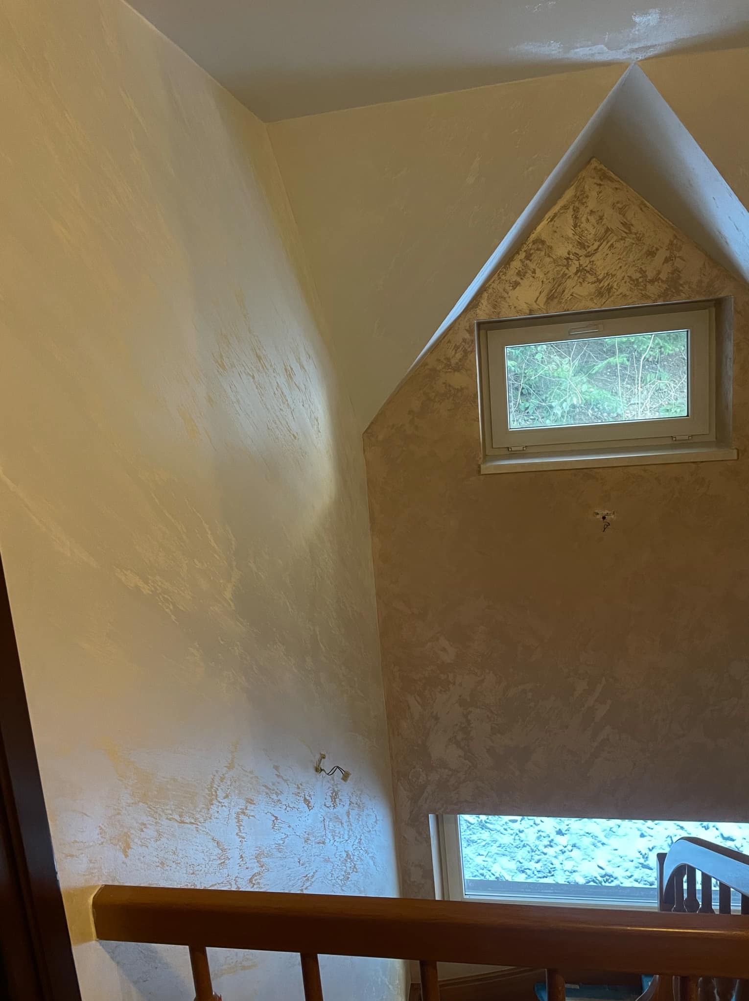 Klatka schodowa w domu z wykończonymi ścianami w dekoracyjnej technice malarskiej, widoczne okno na półpiętrze i fragment drewnianej balustrady schodów.