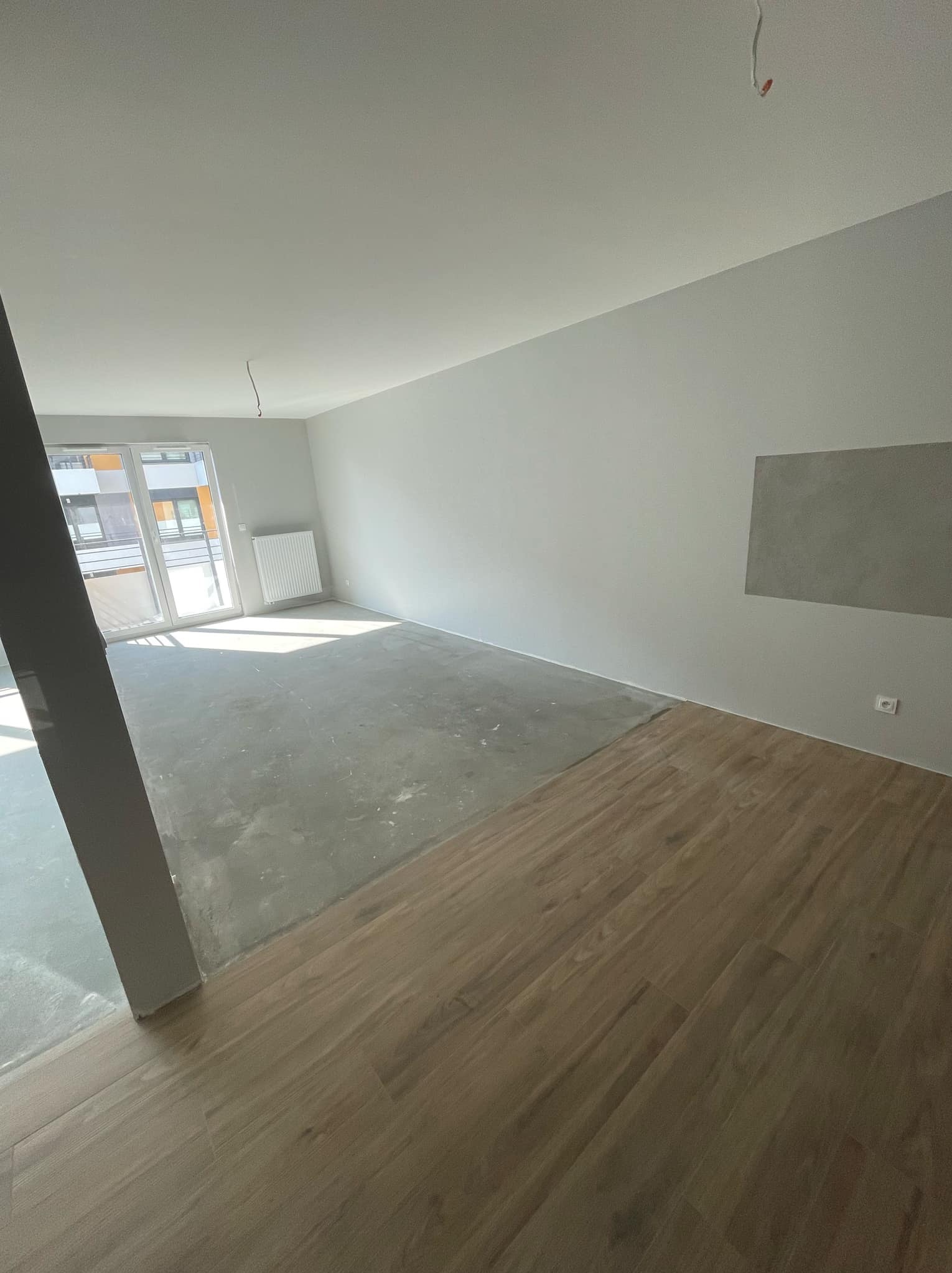 Wnętrze w Tokarni w trakcie prac wykończeniowych: położona częściowo podłoga z paneli drewnopodobnych kontrastuje z surowym, betonowym podłożem. Na ścianie widoczny fragment szarej, niepomalowanej...