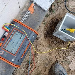 INSTALACJE ELEKTRYCZNE Łukasz Hibszer - Miernik rezystancji uziemienia Sonel z przewodami pomiarowymi podłączonymi do skrzynki uziemiającej w wykopie, obok leżą klucze imbusowe.