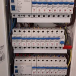 Rozdzielnica elektryczna z zainstalowanymi bezpiecznikami różnicowoprądowymi i nadprądowymi marki Schrack, widoczne przewody w różnych kolorach.