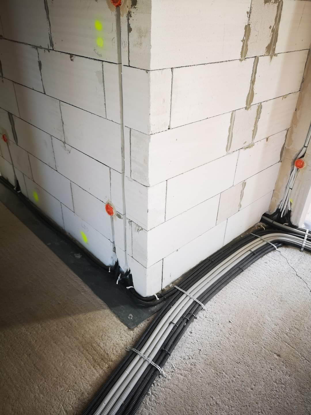 Wewnętrzna instalacja elektryczna w budynku w trakcie budowy, kable w peszlach przymocowane do podłoża metalowymi uchwytami, widoczne puszki instalacyjne w ścianach z betonu komórkowego.