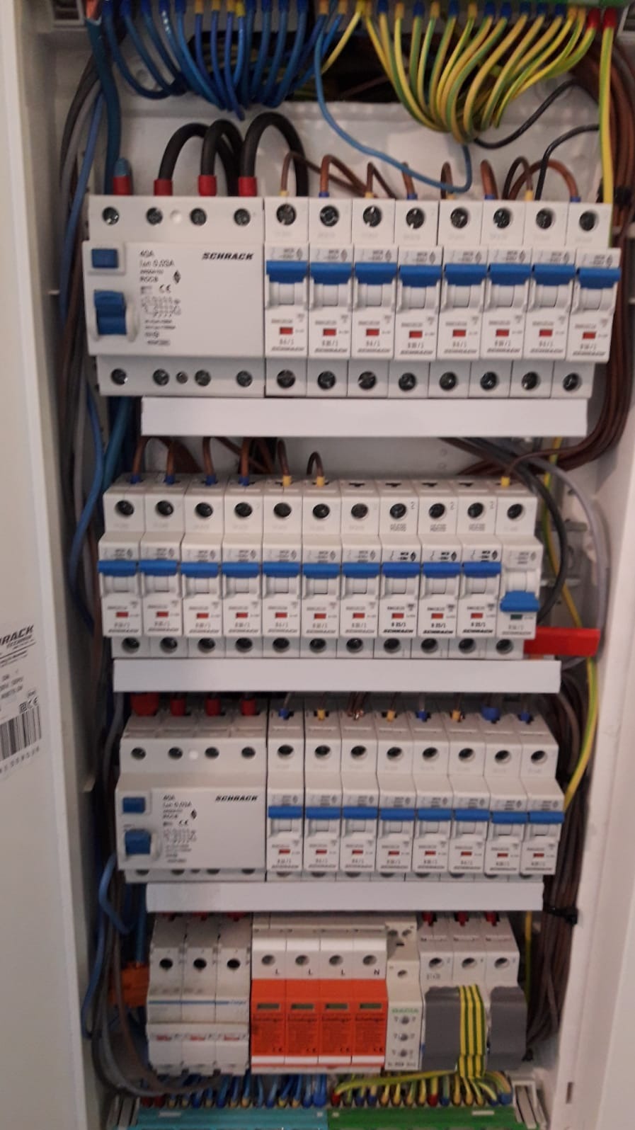 Rozdzielnica elektryczna z zainstalowanymi bezpiecznikami różnicowoprądowymi i nadprądowymi marki Schrack, widoczne przewody w różnych kolorach.
