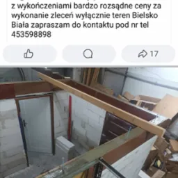 Wnętrze w trakcie prac remontowych: ściany z bloczków, drewniana konstrukcja sufitu, widoczne narzędzia i materiały budowlane, drzwi wejściowe z białą ościeżnicą.