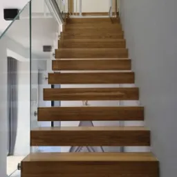 Nowoczesne schody drewniane z balustradą ze szkła hartowanego, zabezpieczenie dla dzieci na górze, widok z dołu.