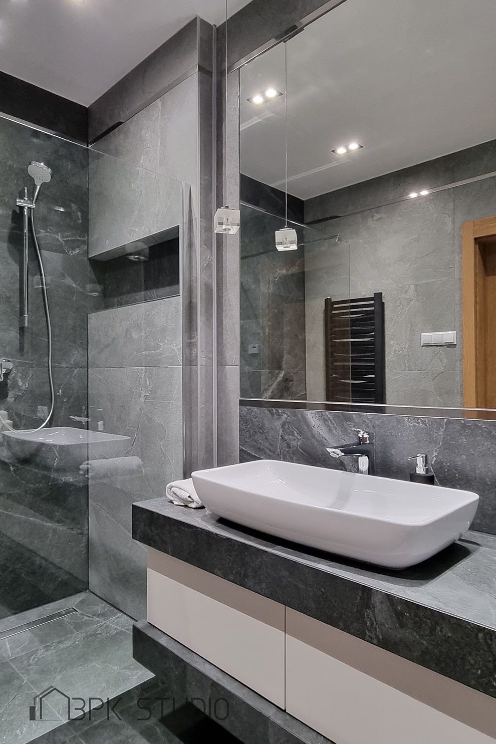 Nowoczesna łazienka w odcieniach szarości z umywalką nablatową, lustrem z wiszącymi lampami i kabiną prysznicową typu walk-in.