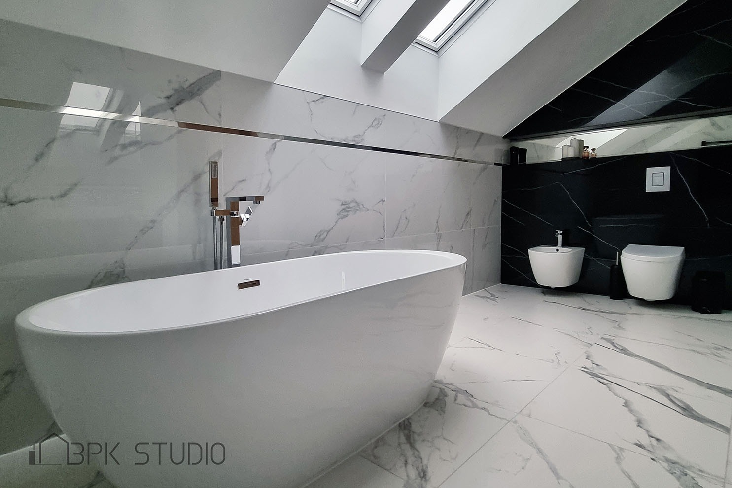Nowoczesna łazienka na poddaszu z białą wolnostojącą wanną, marmurowymi płytkami na ścianach i podłodze, czarną ścianą z toaletą i bidetem oraz oknami dachowymi.