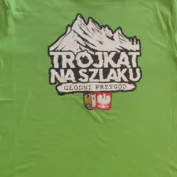 Zielona koszulka z nadrukiem gór, napisu 'Trójkąt na szlaku' i herbów. Widoczna metka Malfini. Koszulka leży na płaskiej powierzchni.