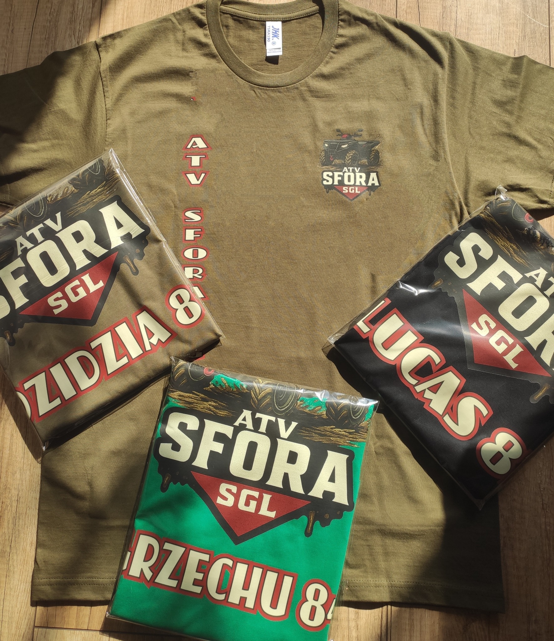 Koszulka khaki z nadrukiem ATV SFORA SGL, obok zapakowane koszulki z imionami Zidzia, Lucas i Rzechu, gotowe do wysyłki. Personalizacja odzieży.