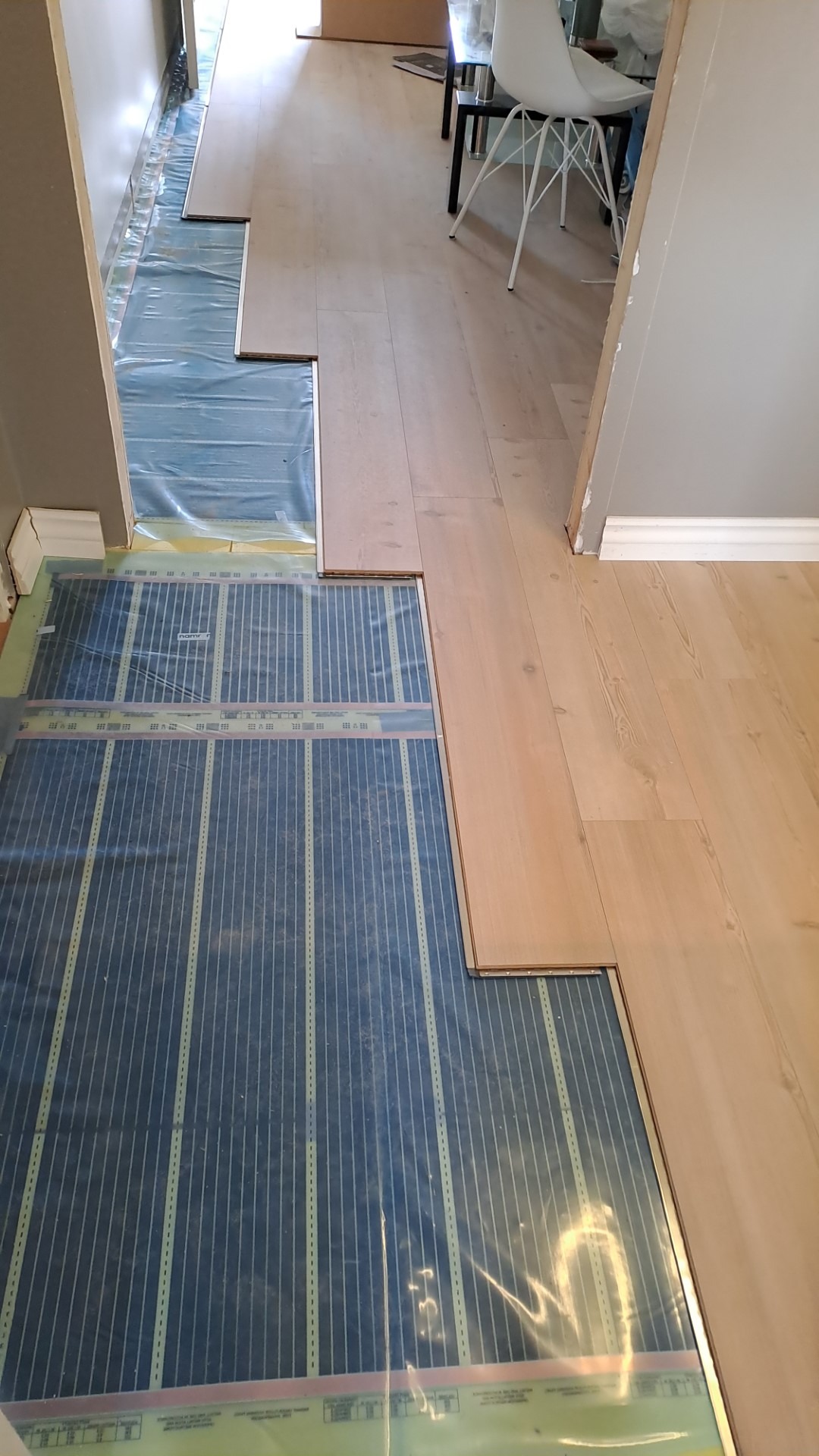 Montaż drewnianej podłogi na folii z ogrzewaniem podłogowym, widoczne panele podłogowe i folia z liniami grzewczymi.