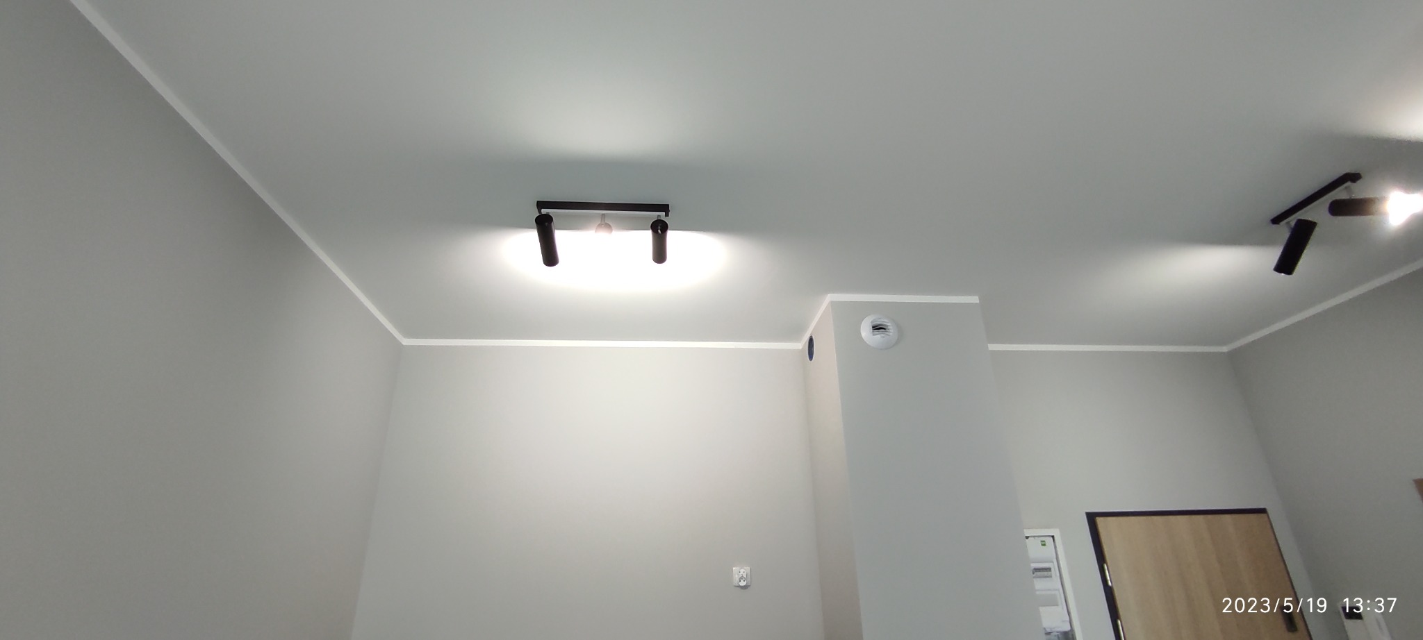 Szare wnętrze z zamontowanym oświetleniem punktowym na suficie, widoczna listwa przysufitowa i kratka wentylacyjna.