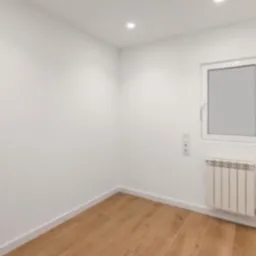 Pusty pokój po remoncie z białymi ścianami, drewnianą podłogą, grzejnikiem i oknem z białymi ramami.