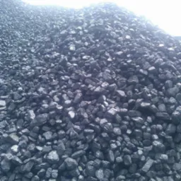 Góra błyszczących, czarnych bryłek węgla, o nieregularnych kształtach i różnej wielkości, oświetlona z góry, tworząca dużą pryzmę.