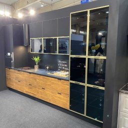 WOJCIECH WYSOCKI - Nowoczesna kuchnia z czarnymi szafkami wiszącymi, drewnianymi szafkami dolnymi i przeszkloną witryną z złotymi ramkami, eksponowana na targach.