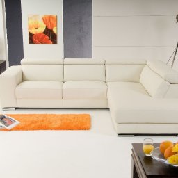 WOJCIECH WYSOCKI - Jasny narożnik z regulowanymi zagłówkami, pomarańczowy dywanik, stolik z owocami i kwiatami, lampa w stylu industrialnym.