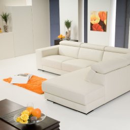 WOJCIECH WYSOCKI - Jasny, skórzany narożnik z regulowanymi zagłówkami w minimalistycznym salonie z pomarańczowym dywanem i owocami na stoliku kawowym.