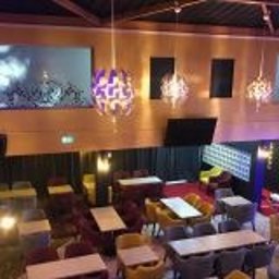 WOJCIECH WYSOCKI - Wnętrze lokalu gastronomicznego z widokiem z antresoli na stoliki i krzesła w różnych kolorach, oświetlone dekoracyjnymi lampami wiszącymi i ekranami.