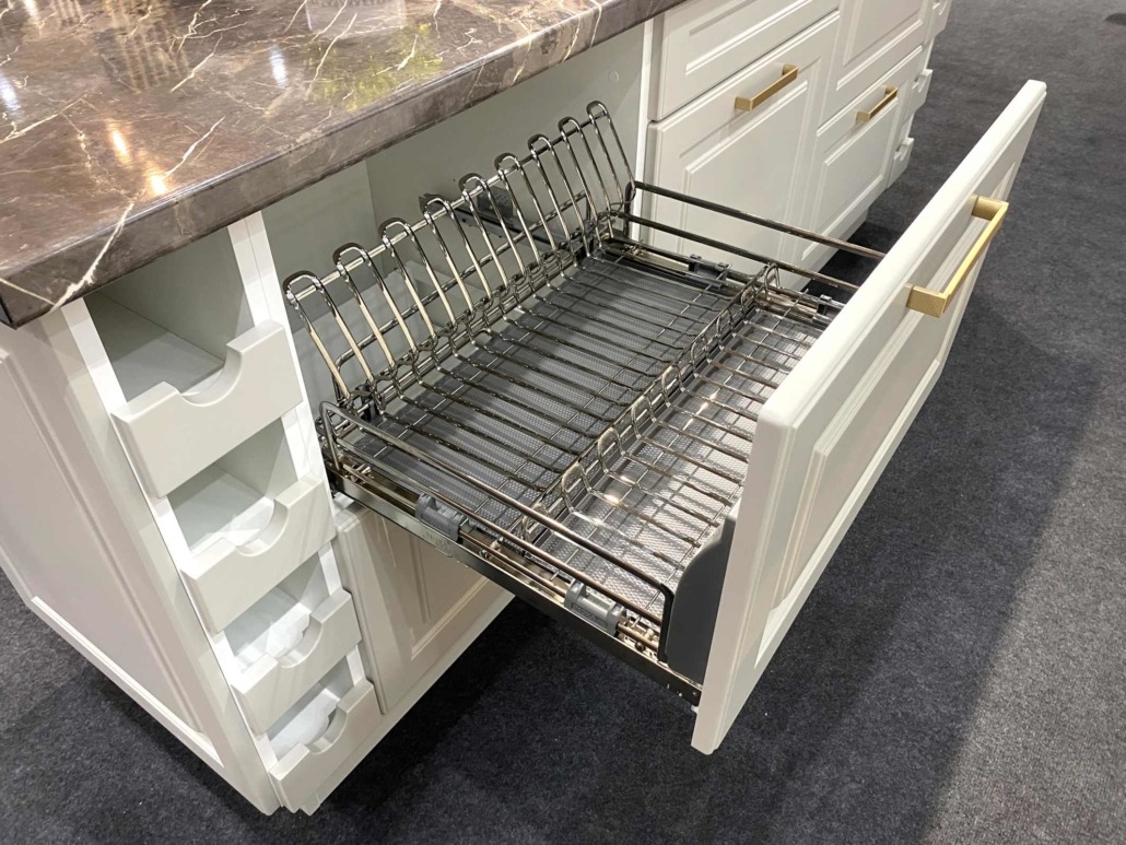 Wysuwana, metalowa suszarka do naczyń w szufladzie białej szafki kuchennej z marmurowym blatem.