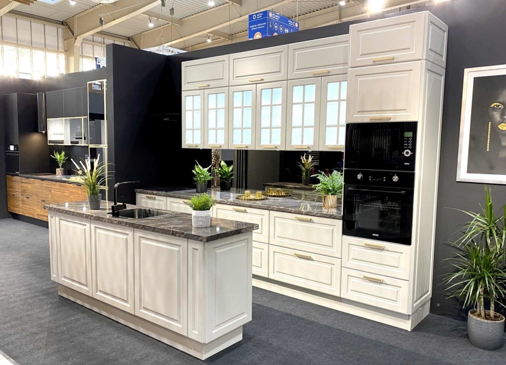 Jasna kuchnia z wyspą i marmurowym blatem, prezentowana w Elblągu na tle czarnej ściany i roślin doniczkowych.