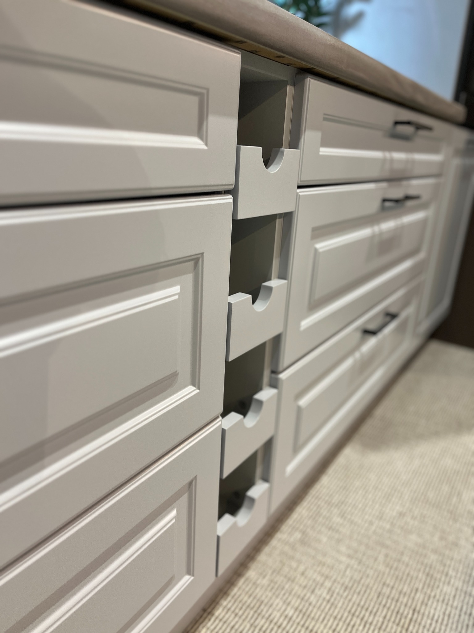 Szare, lakierowane fronty szafek kuchennych z frezowanymi ramkami i czarnymi, podłużnymi uchwytami, dodatkowo widoczne wysuwane półki na butelki.