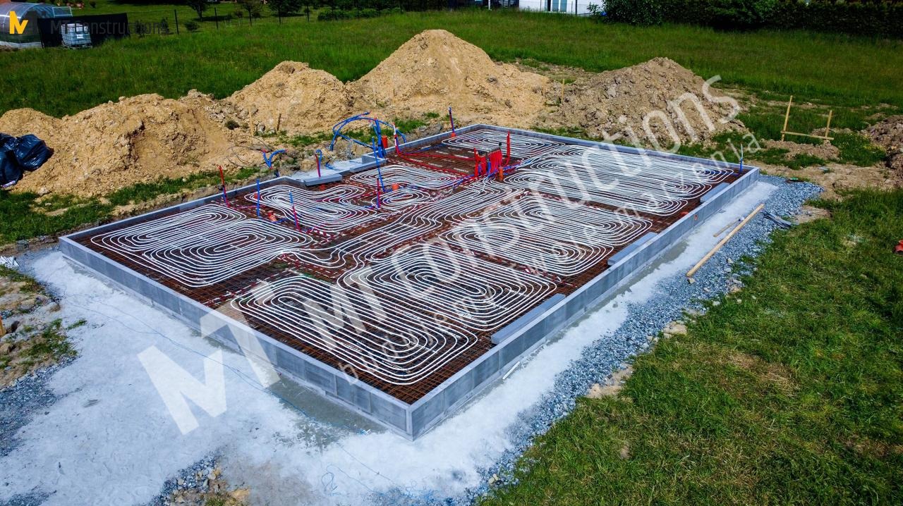 Przygotowany fundament pod dom z rozłożonym systemem ogrzewania podłogowego, widoczne zbrojenie i rury instalacji grzewczej, w tle sterta ziemi.