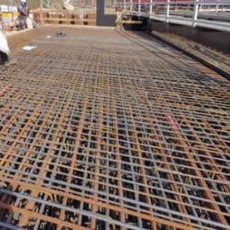 Siatka zbrojeniowa na budowie wiaduktu kolejowego Hennigsdorf, widoczny pracownik w kasku i kamizelce odblaskowej oraz przejeżdżający pociąg