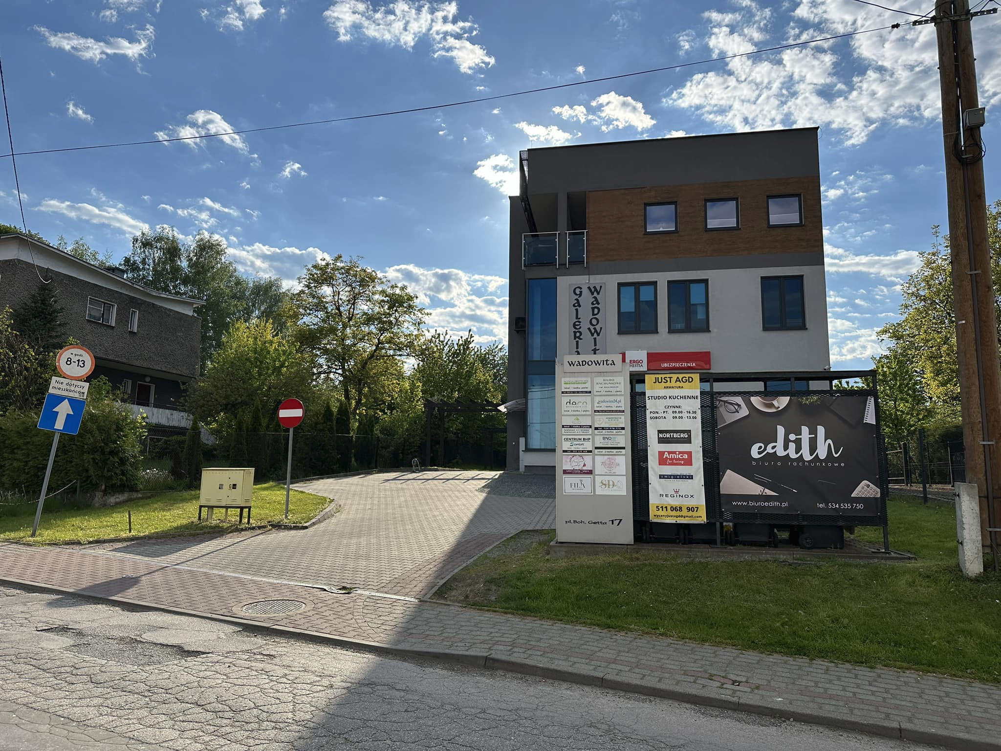 Widok na budynek biurowy z szyldami firm, w tym biura rachunkowego 'edith' z biurkiem i kalkulatorem w tle, w słoneczny dzień.