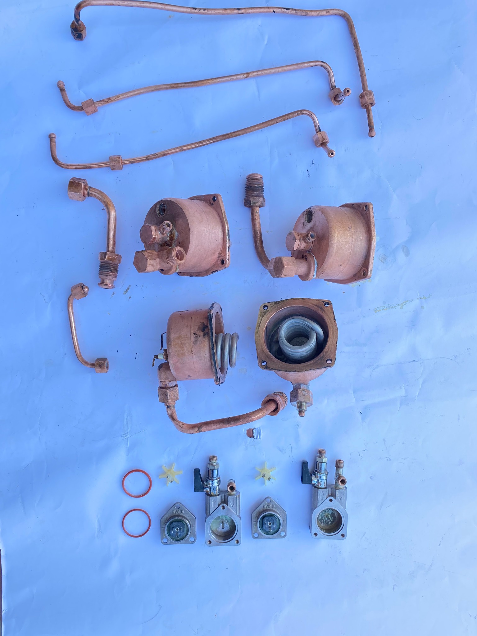 Rozłożone części zamienne do ekspresu do kawy: miedziane rurki, zbiorniki z grzałkami, zawory i uszczelki na białym tle.