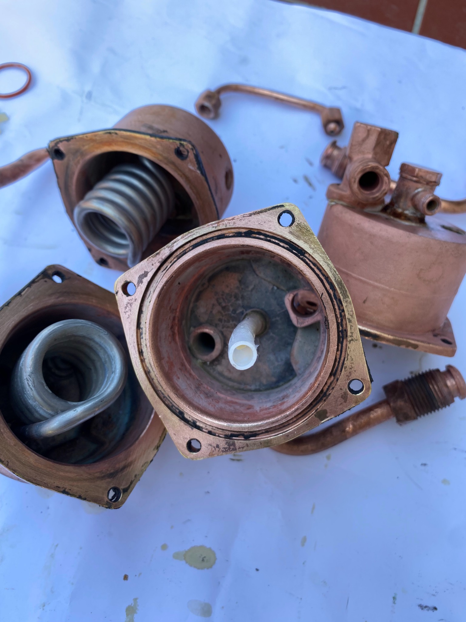 Rozłożone na części elementy ekspresu do kawy, miedziane i metalowe, widoczne grzałki i obudowy, na białym tle.