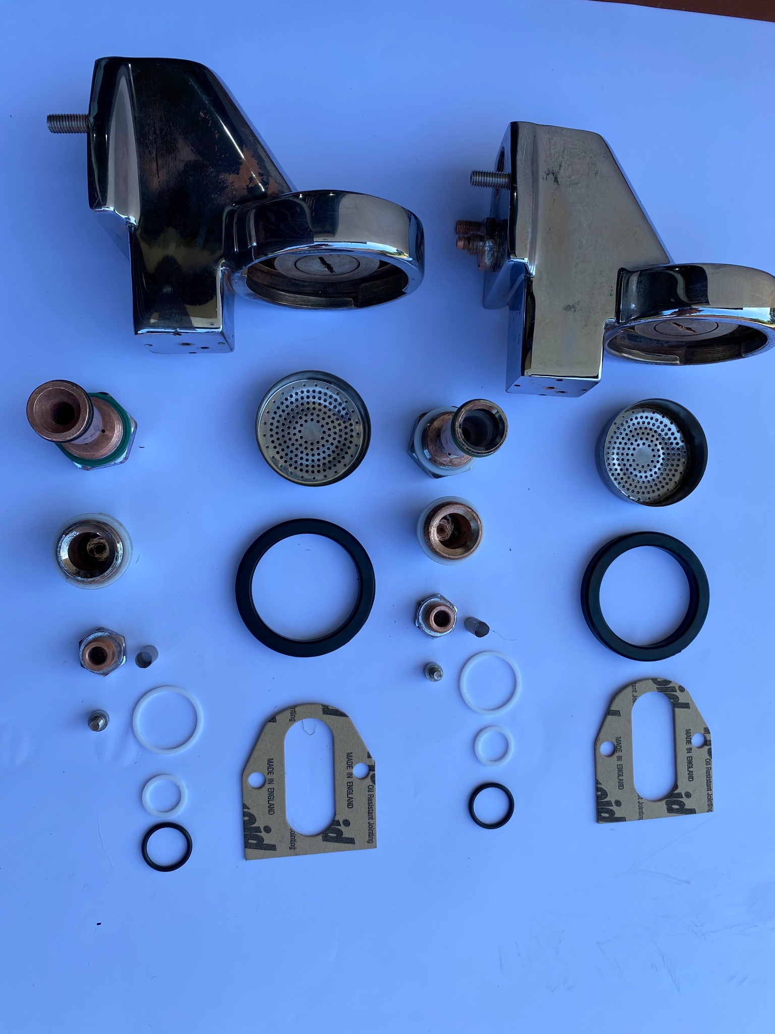 Rozłożone na białym tle chromowane elementy ekspresu do kawy, w tym dysze, uszczelki, sitka i śruby, widoczne ślady użytkowania na obudowach.