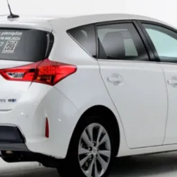 Biała Toyota Auris Hybrid z naklejoną reklamą na tylnej szybie, zawierającą hasło '#Robimy dla was pieniądze', numer telefonu i kod QR.