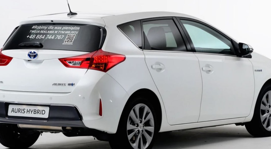 Biała Toyota Auris Hybrid z naklejoną reklamą na tylnej szybie, zawierającą hasło '#Robimy dla was pieniądze', numer telefonu i kod QR.