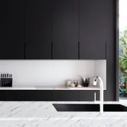 Nowoczesna kuchnia w Krakowie z czarnymi szafkami bez uchwytów, białym blatem i marmurowym wykończeniem wyspy kuchennej, widok na zieleń za oknem.