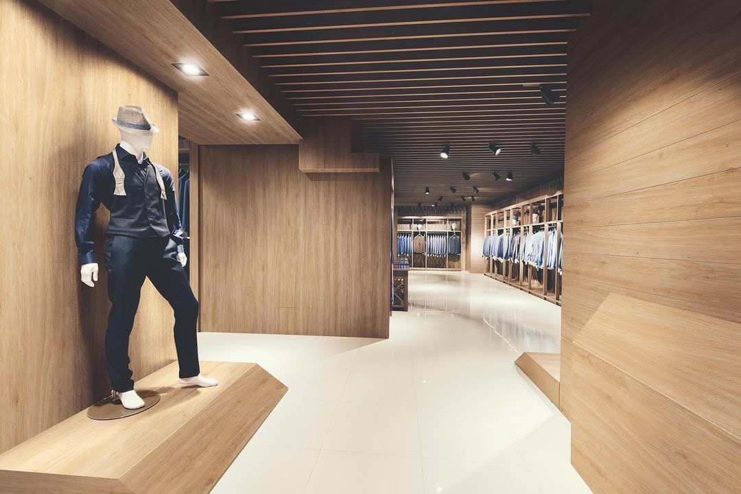 Wnętrze butiku z drewnianymi panelami ściennymi i podświetlanym sufitem z widocznym manekinem w eleganckim garniturze i kapeluszu.