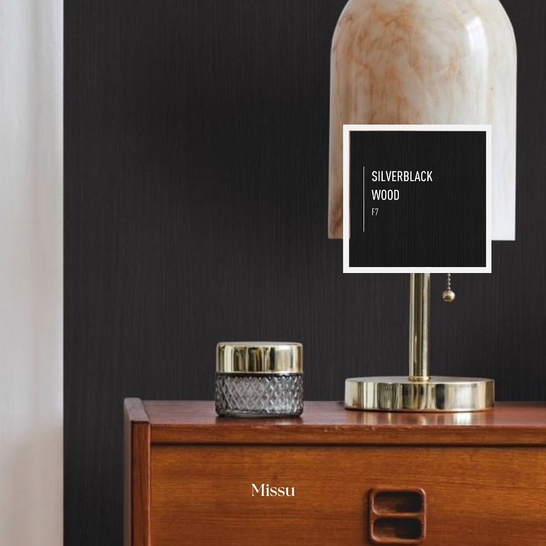 Drewniana komoda w odcieniach brązu z lampą z marmurowym abażurem i szklanym pojemnikiem z metalową pokrywką na blacie, na tle ściany z ciemną tapetą.