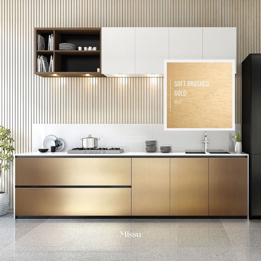 Nowoczesna kuchnia z frontami szafek w kolorze szczotkowanego złota, białe szafki wiszące, drewniane półki, płyta grzewcza z garnkiem, minimalistyczny design, reklama koloru farby Soft Brushed Gold...